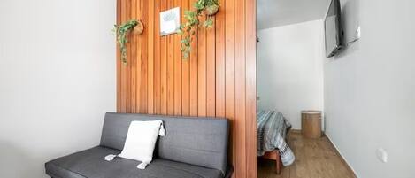Une pièce moderne avec un canapé gris, un mur recouvert de panneaux en bois et un téléviseur fixé au mur.