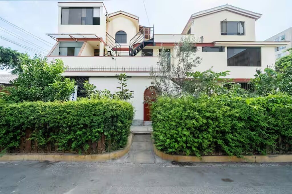 Un edificio residencial de dos pisos con una entrada central, una escalera y un pequeño porche.