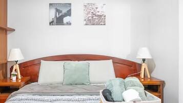 Un lit bien fait, recouvert d’une couverture grise, deux lampes de chevet, une petite table de chevet avec une lampe et un cadre photo fixé au mur.