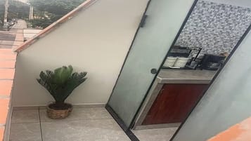 Un coin de pièce avec un sol carrelé, une plante en pot, un meuble avec une porte en verre et un mur également carrelé.