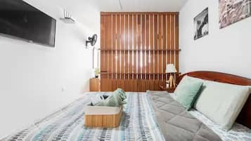 A bedroom with a bed, a wooden headboard, a wall-mounted TV, and a bedside lamp.