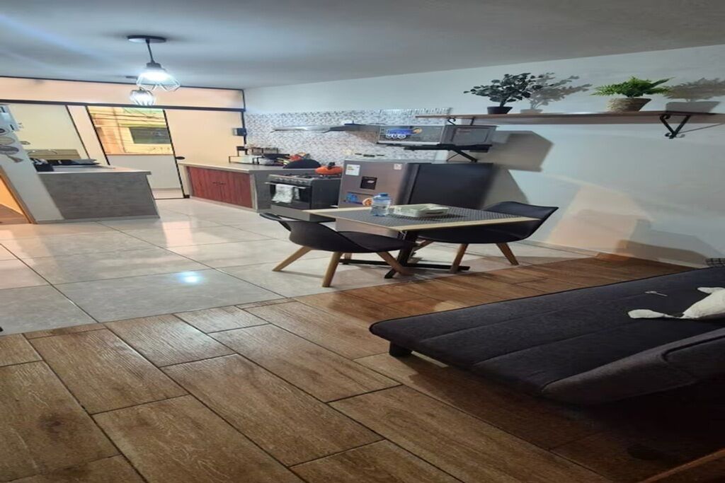 A modern kitchen with a dining area, wooden flooring, and a sofa.
