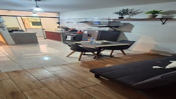 A modern kitchen with a dining area, wooden flooring, and a sofa.