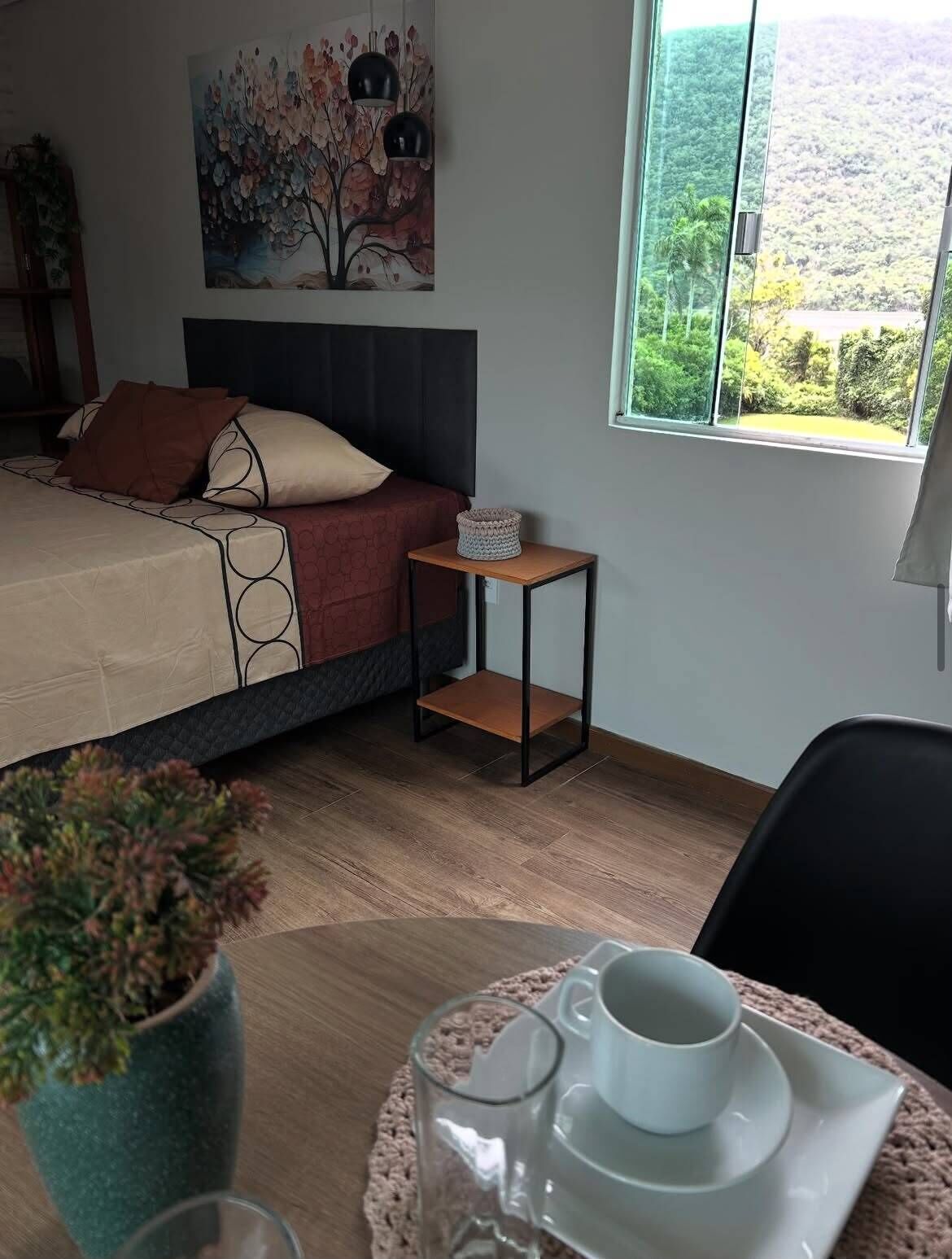 Ein Schlafzimmer mit Bett, Nachttisch, Fenster mit Blick und kleinem Tisch mit Tasse und Untertasse.