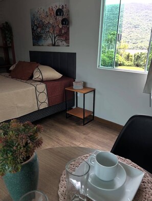 Ein Schlafzimmer mit Bett, Nachttisch, Fenster mit Blick und kleinem Tisch mit Tasse und Untertasse.