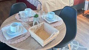 A hotel room with a bed, a TV mounted on the wall, a painting, and a dining area set up with a table and chairs. - Guest house 700 meters from Moçambique beach and 500 meters from the state park. (Florianópolis)