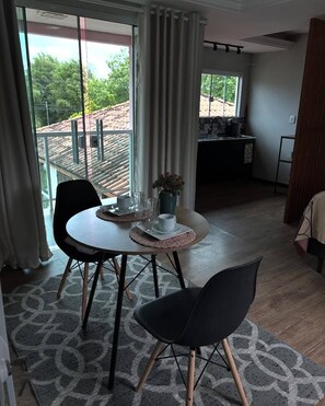 A dining area with a round table, two chairs, a vase with flowers, and a view of a balcony with a tiled roof. - Guest house 700 meters from Moçambique beach and 500 meters from the state park. (Florianópolis)