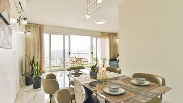 Comedor con mesa dispuesta para cuatro, sillas, plantas en macetas y vista de la ciudad a través de amplios ventanales.