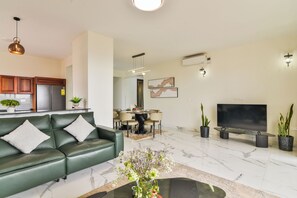 Una sala de estar moderna con un sofá de cuero verde, un comedor con mesa y sillas, un televisor de pantalla plana y una cocina con armarios de madera.