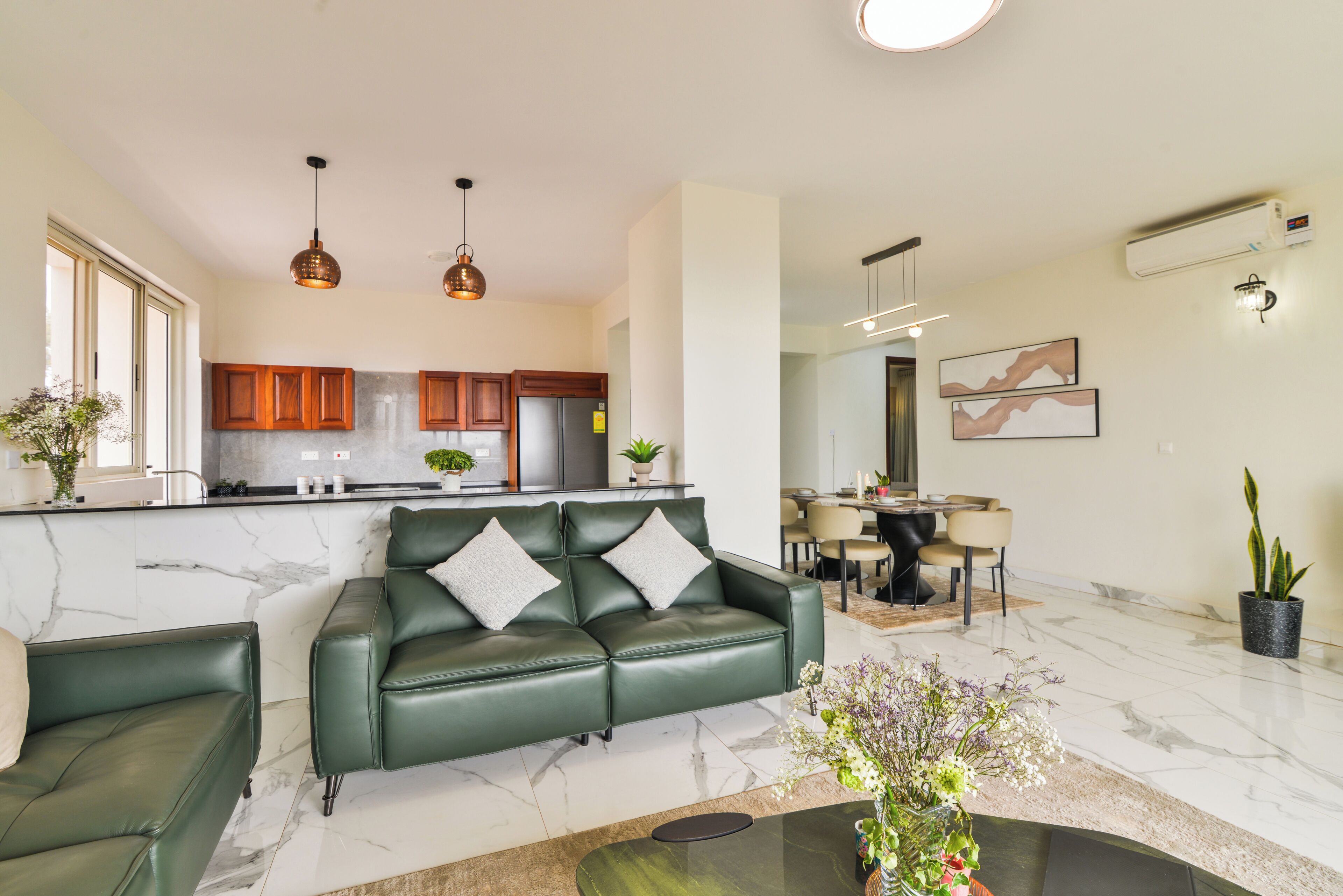 Uma sala de estar moderna com um sofá de couro verde, uma área de jantar com uma mesa redonda e uma cozinha com armários de madeira.