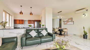 Una sala de estar moderna con un sofá de cuero verde, un comedor con mesa redonda y una cocina con armarios de madera.