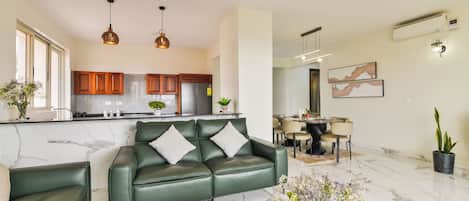 Un salon moderne avec un canapé en cuir vert, un coin repas doté d’une table ronde et une cuisine avec des meubles en bois.