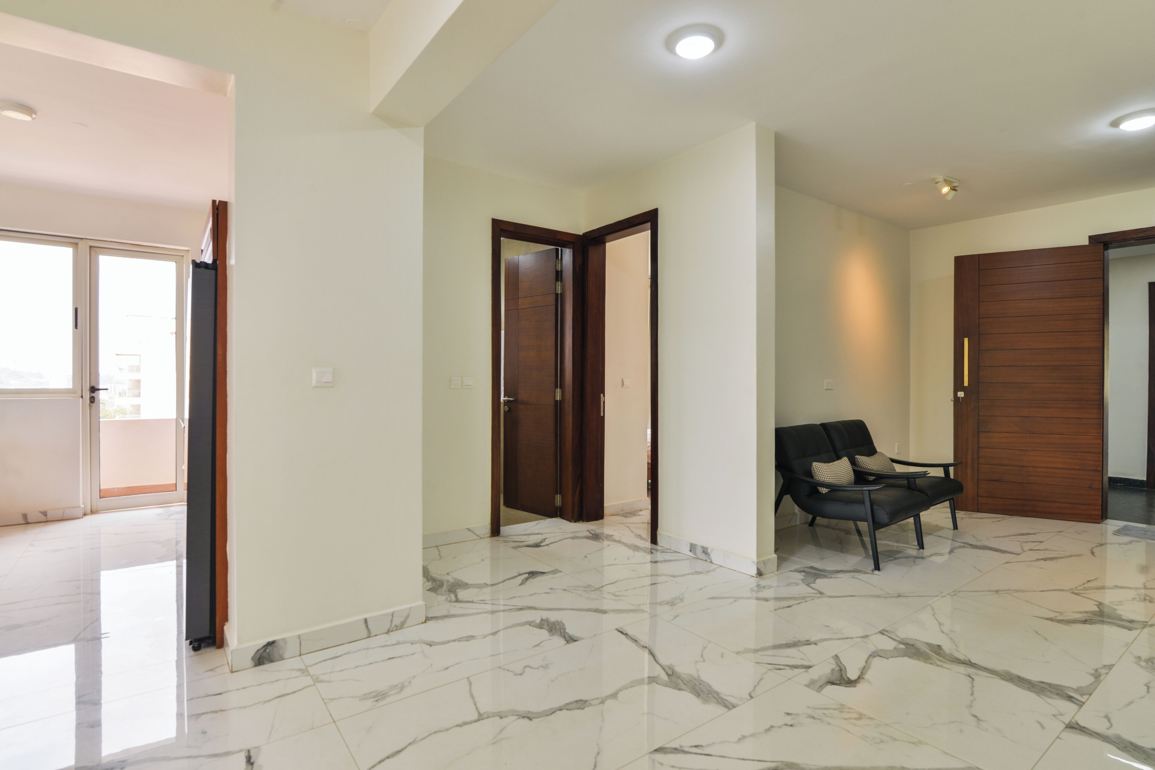 Un pasillo amplio con piso de mármol, una puerta de madera y una silla negra.