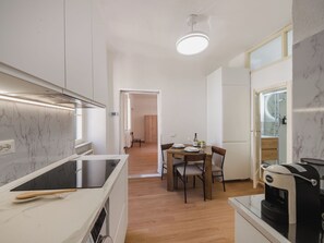 Une cuisine moderne dotée d’une cuisinière intégrée, un coin repas avec une table et des chaises, et une vue sur le salon grâce à une porte ouverte.