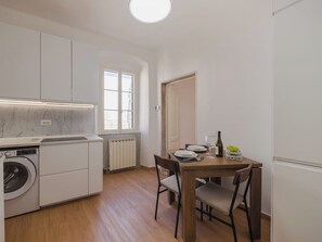 Une cuisine compacte équipée d’un lave-linge, d’une table à manger avec des chaises et d’une fenêtre donnant sur un paysage agréable.