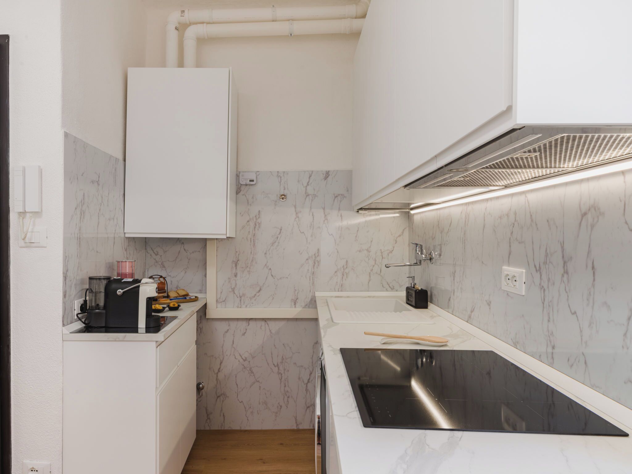 A compact kitchen with white cabinets, a black sink, and a marble backsplash.