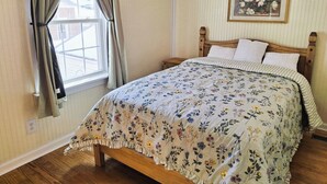A bedroom with a wooden bed, floral bedding, a window with curtains, and a framed picture on the wall.