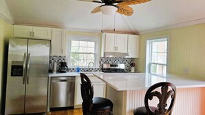 A kitchen with a central island, stainless steel appliances, and a ceiling fan with leaf-shaped blades.