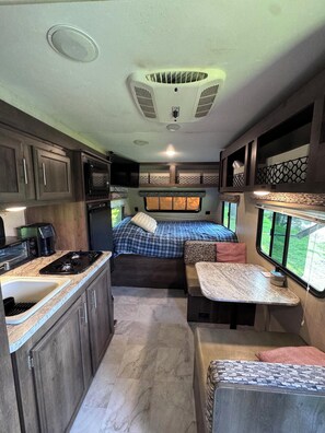 Ein kompaktes Wohnmobil-Interieur mit Küchenzeile, einem Bett mit Fenster und einer kleinen Sitzecke.