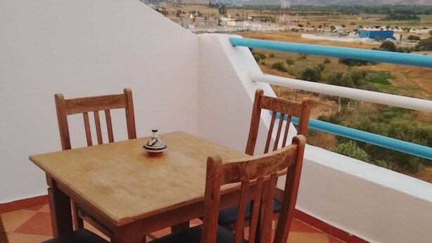 A balcony with a wooden table and chairs, a view of distant mountains, and a checkered floor. - Perfect 2-bedroom house in Chefchaouen for a relaxing stay (Chefchaouen)