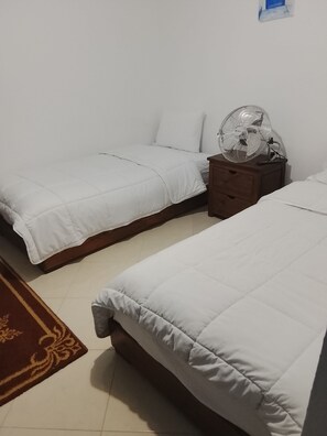 Ein Zimmer mit zwei Betten, einem Nachttisch aus Holz und einem gemusterten Teppich.