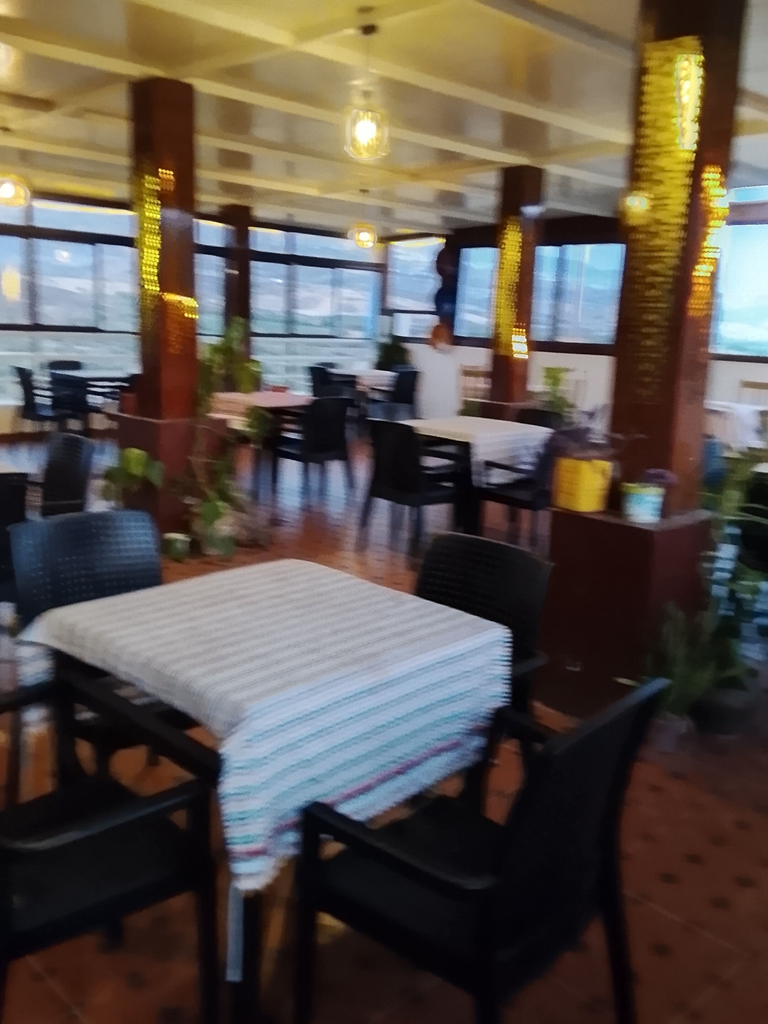 A restaurant interior with tables and chairs, large windows, and decorative pillars.