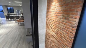Un intérieur moderne avec un mur en briques, un coin repas avec des tables et des chaises, et une vue sur l’extérieur.