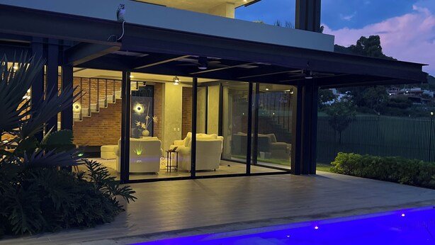 A modern house with a swimming pool, glass doors leading to an interior with a fireplace, and a patio area.