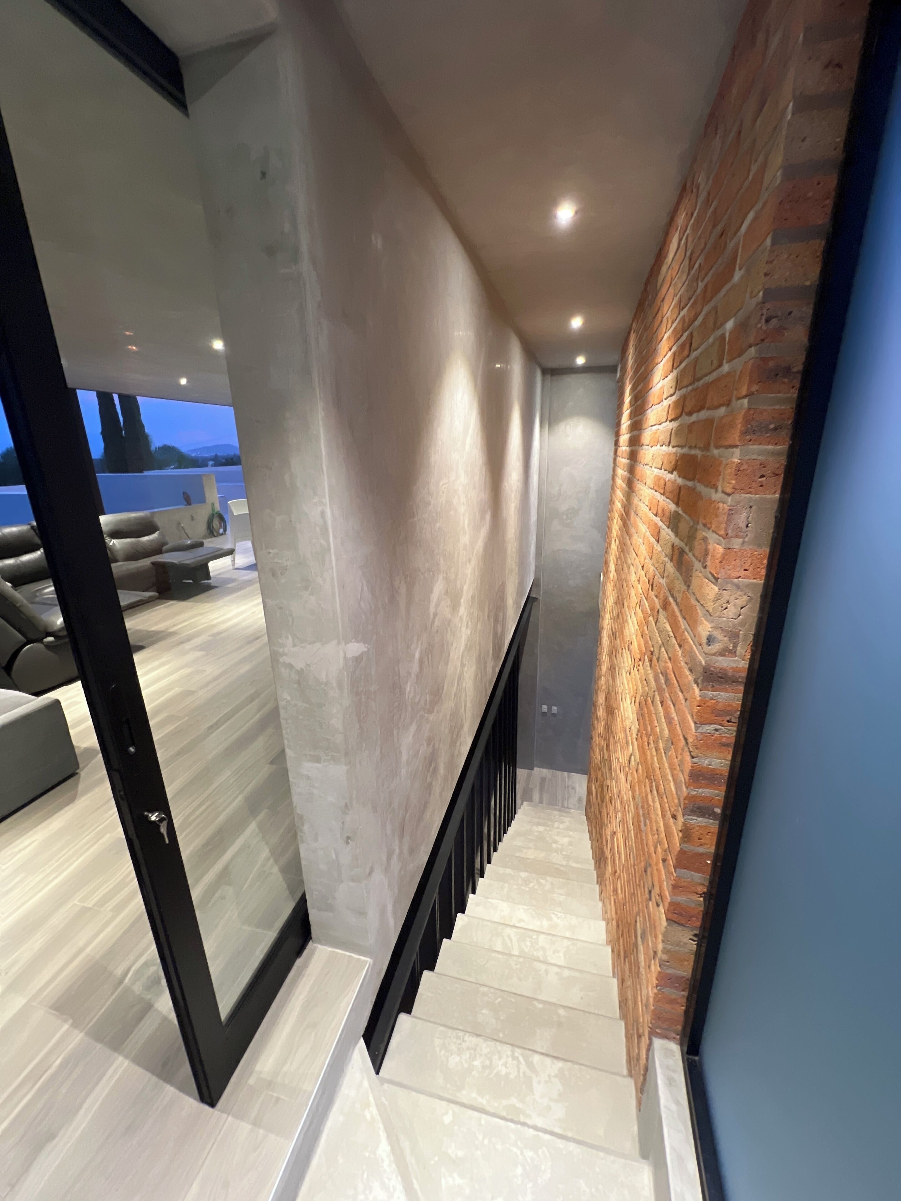 Un interno moderno con una scala, un muro in mattoni e una vista attraverso una porta di vetro.