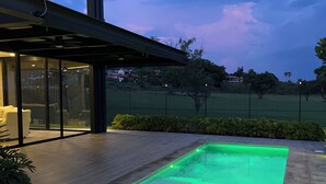 Un espace piscine extérieur moderne, doté d’une structure en verre et d’une terrasse en bois.