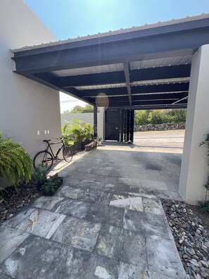 Una entrada cubierta con una bicicleta estacionada a la izquierda, un muro de piedra al fondo y un camino pavimentado que conduce a un edificio.