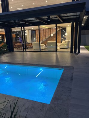 A modern house with a swimming pool, a covered outdoor seating area, and a staircase leading to an upper level.