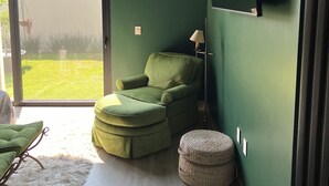 A room with a green wall, a green armchair, a small ottoman, a floor lamp, and a television mounted on the wall.