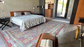 Et moderne soveværelse med en stor seng, et skrivebord og en stol. Der er udsigt til en balkon med gelænder.