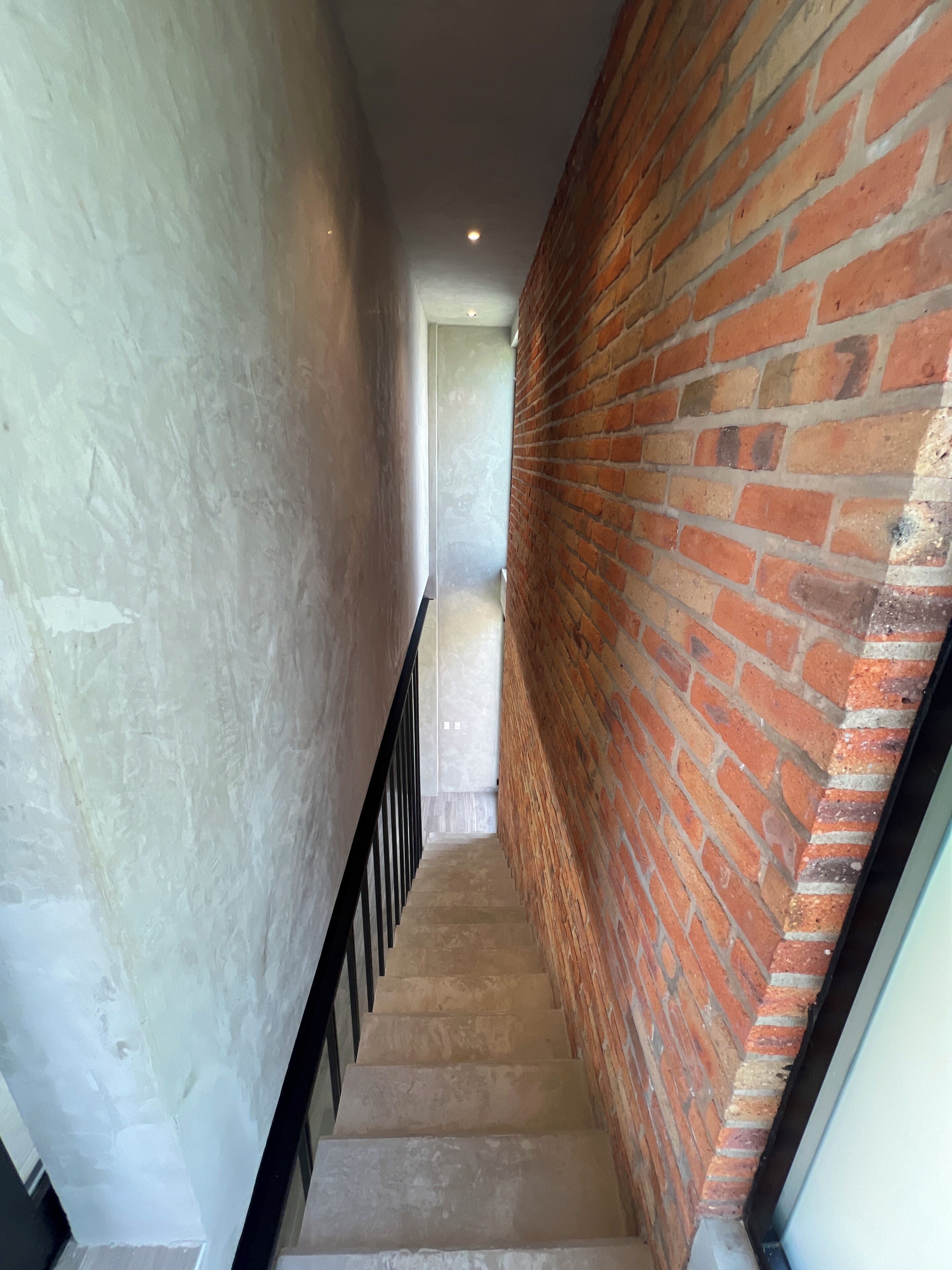 A narrow stairway with a brick wall on one side and a plain wall on the other, leading to a doorway at the top.
