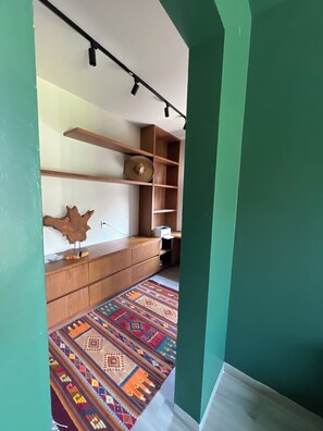 A room with a wooden cabinet, a patterned rug, and a wall-mounted shelf with a hat.
