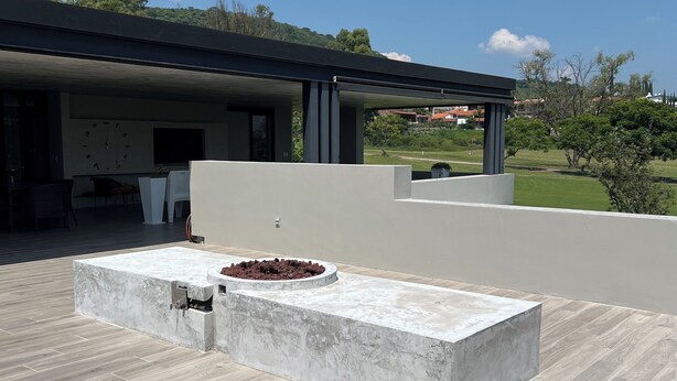 Une terrasse extérieure dotée d’un foyer intégré et d’un espace salon, entourée d’une maison moderne et offrant une vue sur un paysage verdoyant.