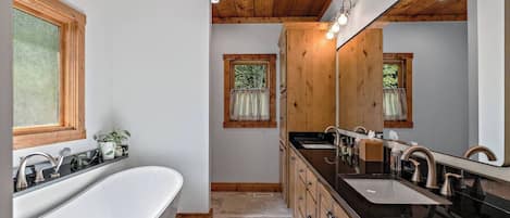 A modern bathroom with a freestanding bathtub, a double sink vanity, wooden cabinetry, and a large mirror.