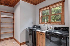 A compact kitchen with a built-in washer and dryer, a wooden shelf unit, and a window with a view of trees. - Stunning Mountain Views/Hot Tub/Fireplaces /3 Kings (Blue Ridge)