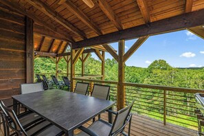 A wooden deck with a table and chairs, overlooking a forested landscape. - Stunning Mountain Views | Hot Tub | Fireplaces | 3 Kings (Blue Ridge)