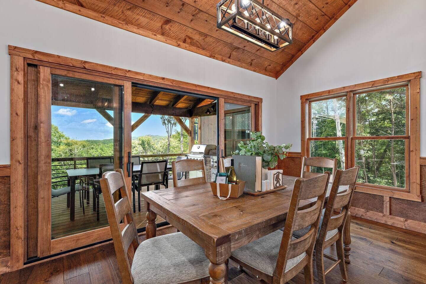 A wooden dining table with chairs, a grill, and a view of the outdoors.