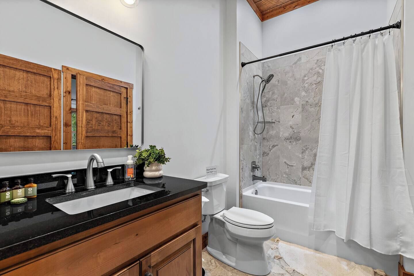 A bathroom with a wooden vanity, a sink, a toilet, a bathtub, and a shower curtain.