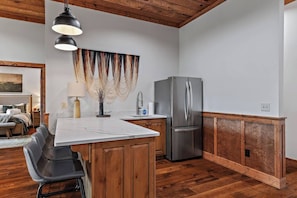 A modern kitchen with a stainless steel refrigerator, wooden cabinets, a marble countertop, and a hanging light fixture. - Stunning Mountain Views | Hot Tub | Fireplaces | 3 Kings (Blue Ridge)