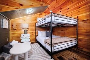 A bunk bed with a nightstand and a small table, a lamp, and a rug in a wooden room. - Newly Renovated Modern 4BR Cabin w/Indoor Pool ☆ Hot Tub ☆ Theater ☆Arcade Games (Sevierville)