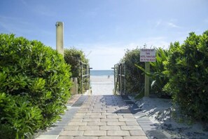 A paved pathway leading to a beach with a sign indicating hotel furniture is to be taken to the beach. - Newly updated king studio perfect for honeymooners (Daytona Beach)
