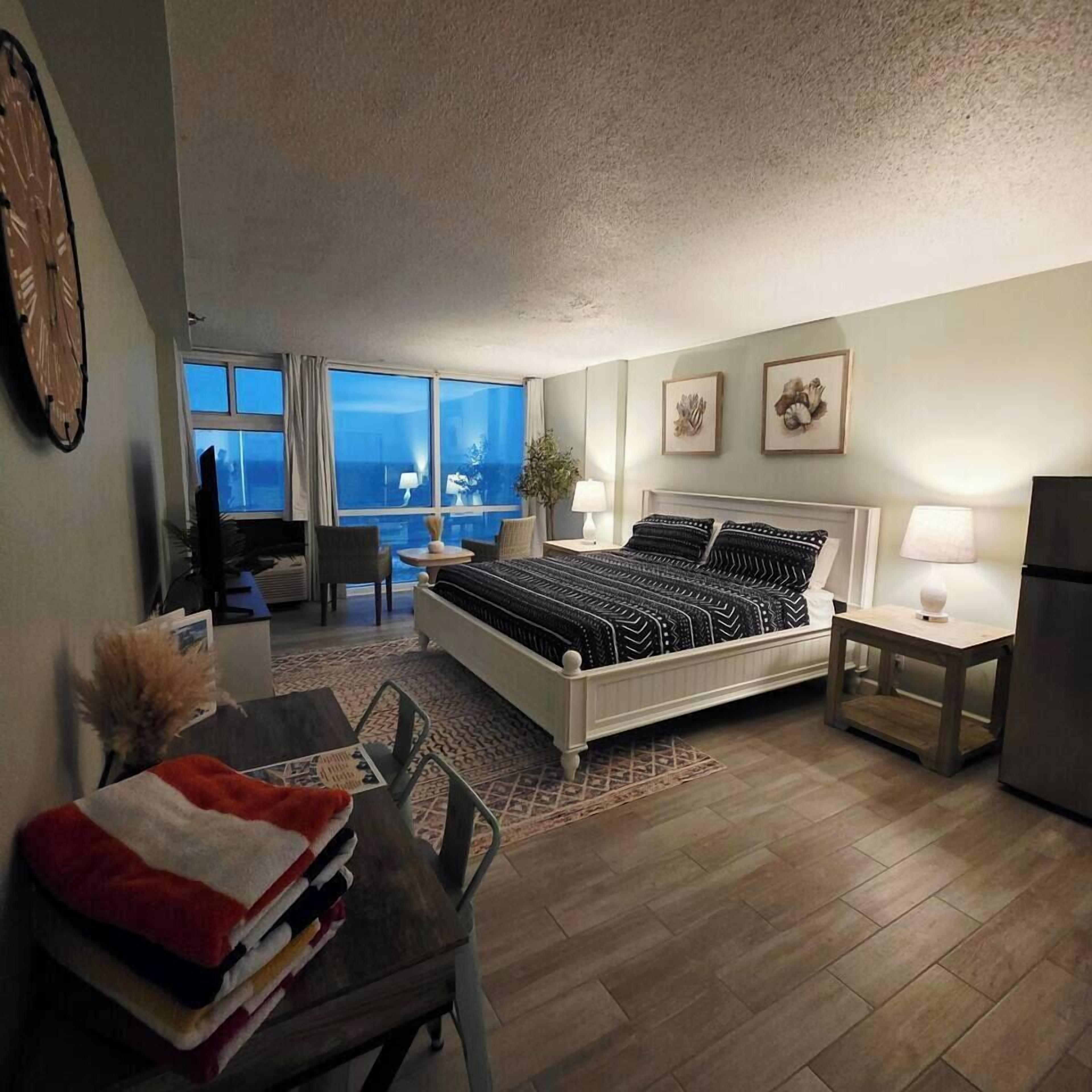 Ein Hotelzimmer mit Bett, Schreibtisch, Stuhl, Esstisch und Blick auf den Ozean.