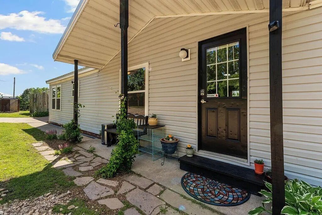 A residential property with a front porch, a black door, and a small garden area with potted plants.