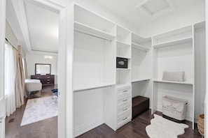 Ein begehbarer Kleiderschrank mit offenen Regalen, eine dunkelbraune Kommode und ein weißer Fellteppich.