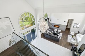 Ein modernes Interieur mit Treppe, einer Kristallleuchter, einem Kamin und Blick auf Grünflächen.