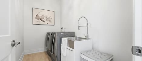 A compact laundry area with a washing machine, a sink, and a small storage bin.